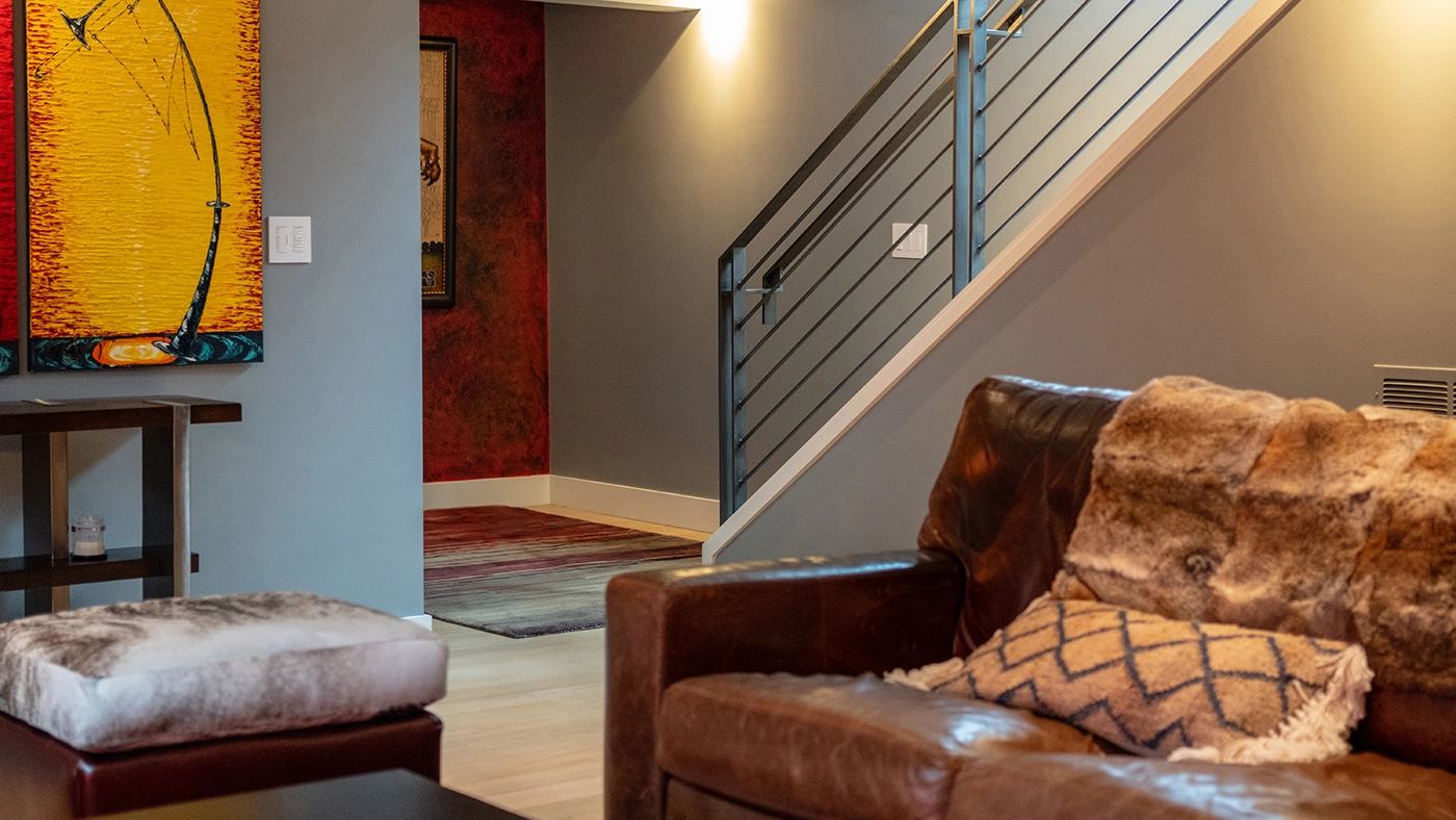 Modern cozy living space with leather sofa, vibrant artwork, and elegant staircase.