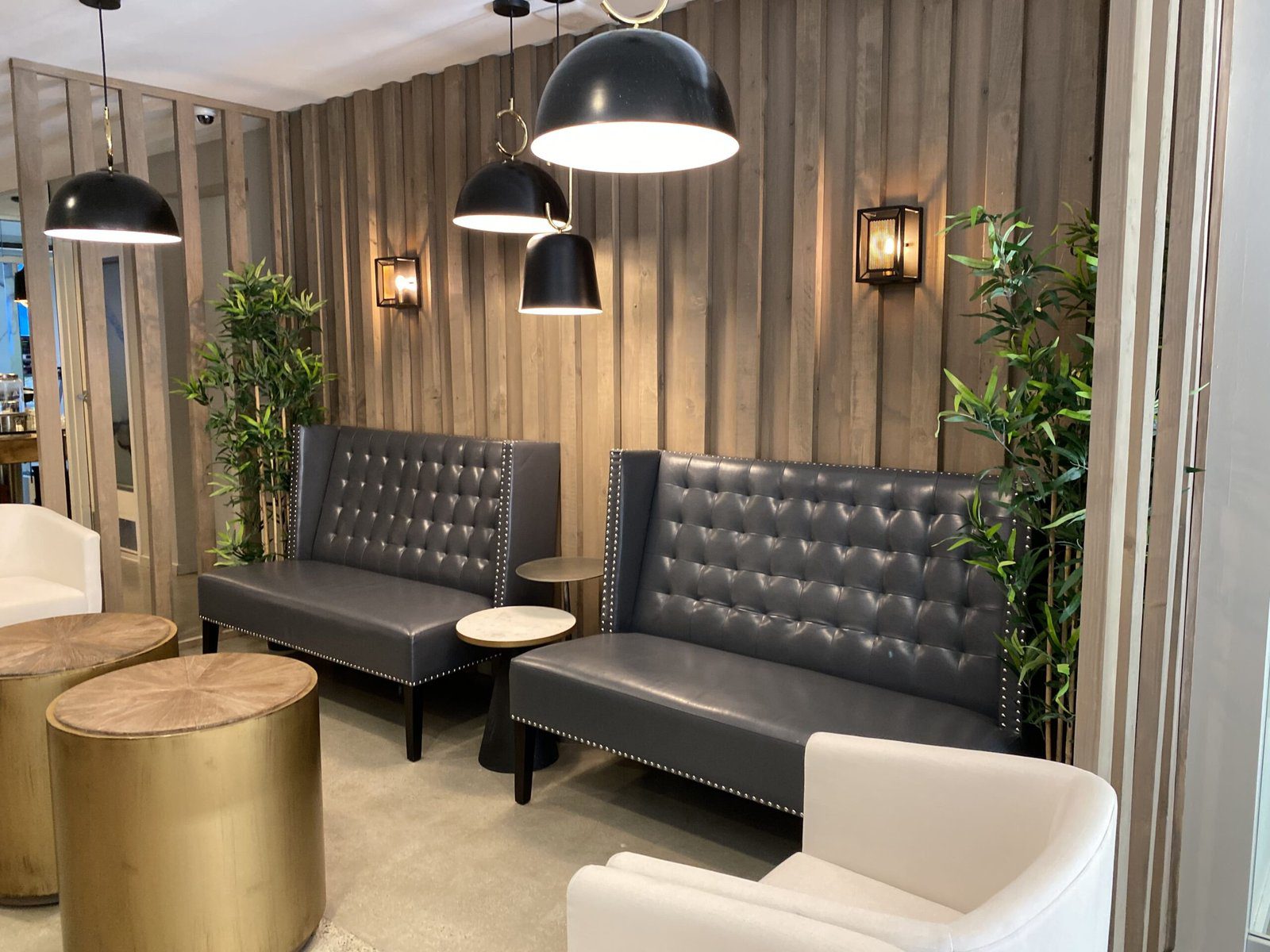 Detail of lounge corner with charcoal tufted sofa, potted plant and wood slat backdrop.
